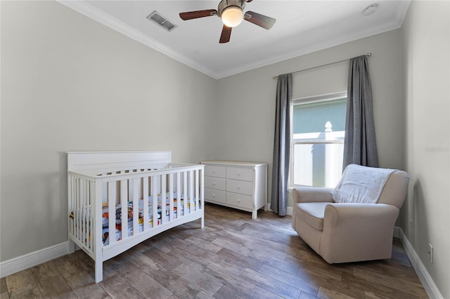 bedroom featuring wood finished floors, baseboards, visible vents, ornamental molding, and a crib