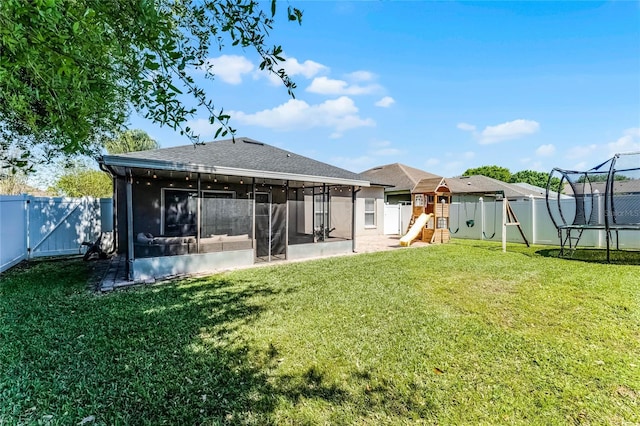 rear view of house with a fenced backyard, a yard, a trampoline, and a sunroom