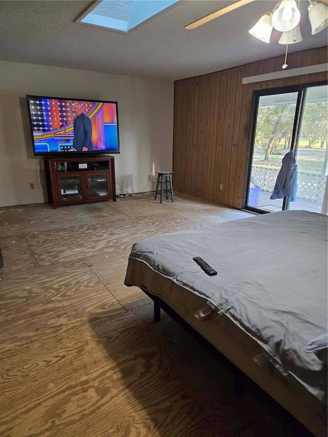 bedroom featuring wooden walls, a skylight, a textured ceiling, a ceiling fan, and access to outside