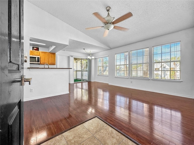 unfurnished living room featuring plenty of natural light, wood-type flooring, vaulted ceiling, and ceiling fan with notable chandelier