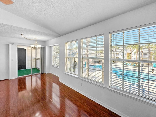 unfurnished room with a notable chandelier, lofted ceiling, a textured ceiling, wood finished floors, and baseboards