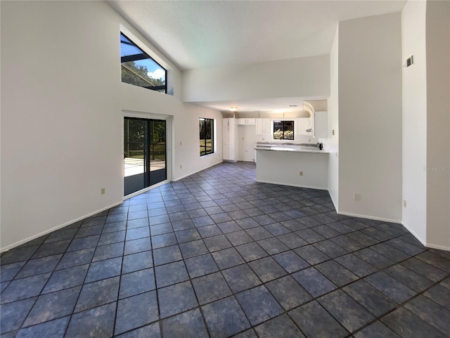 unfurnished living room featuring dark tile patterned floors, baseboards, and high vaulted ceiling