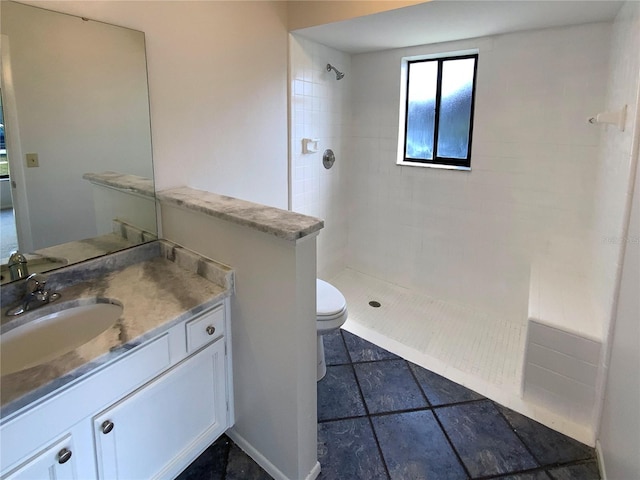 bathroom featuring toilet, tiled shower, and vanity