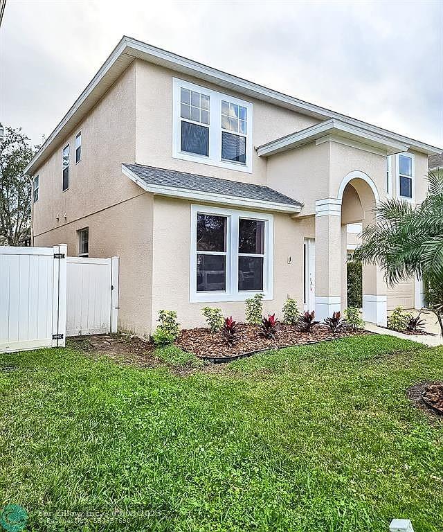 traditional-style home featuring a front yard, fence, and stucco siding