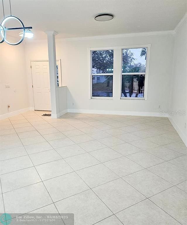 spare room featuring baseboards, ornamental molding, light tile patterned flooring, and ornate columns