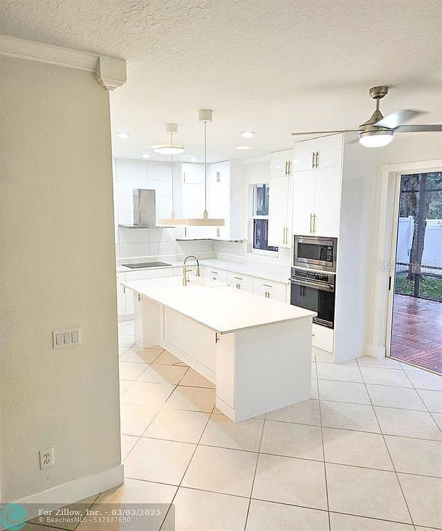 kitchen with a sink, white cabinetry, stainless steel appliances, light countertops, and ceiling fan