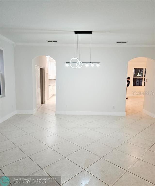 spare room with visible vents, arched walkways, and crown molding