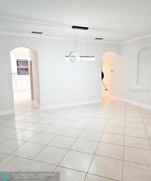 spare room featuring light tile patterned floors, visible vents, arched walkways, and ornamental molding