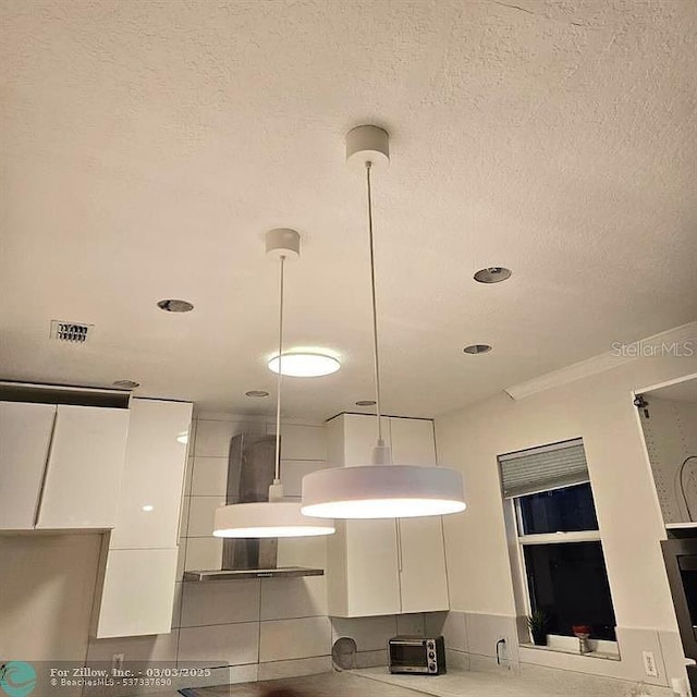 room details with visible vents, white cabinetry, wall chimney range hood, a toaster, and a textured ceiling