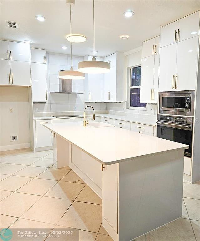 kitchen featuring a center island with sink, a sink, white cabinetry, appliances with stainless steel finishes, and light tile patterned floors