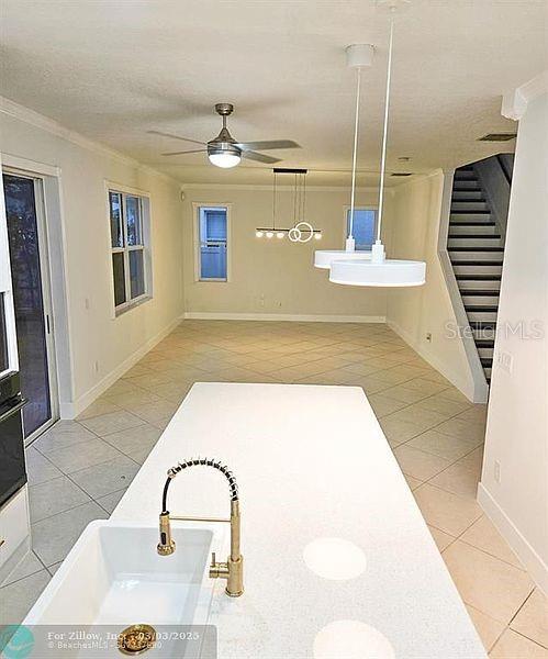 interior space with light tile patterned floors, baseboards, crown molding, and a ceiling fan