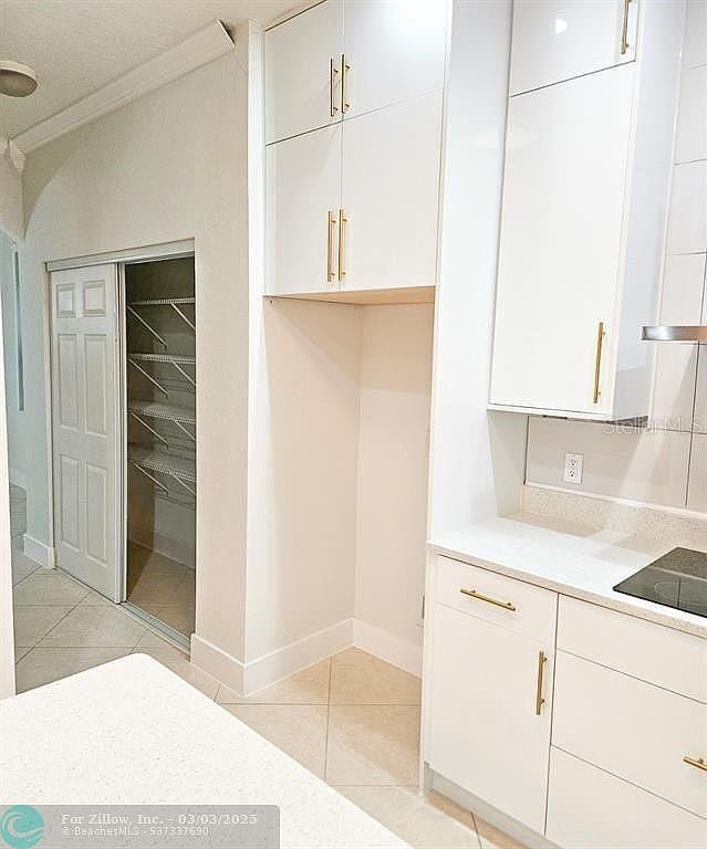 kitchen featuring light tile patterned flooring, crown molding, white cabinets, black electric stovetop, and light countertops