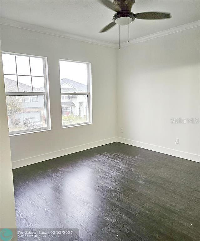 unfurnished room with dark wood finished floors, a ceiling fan, baseboards, and ornamental molding