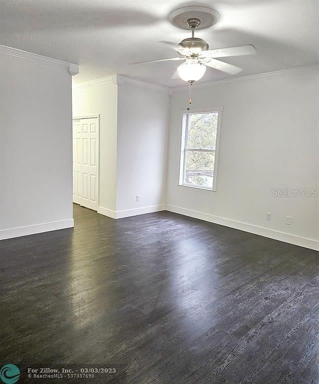 unfurnished room featuring baseboards, dark wood-style flooring, ceiling fan, and crown molding