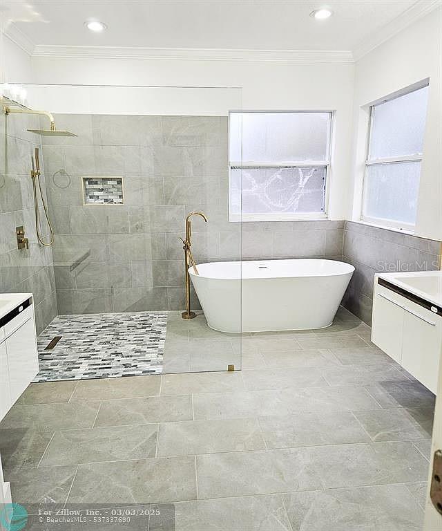 bathroom with tile walls, walk in shower, ornamental molding, a freestanding tub, and vanity