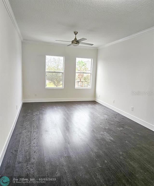 unfurnished room with a ceiling fan, baseboards, dark wood-type flooring, a textured ceiling, and crown molding