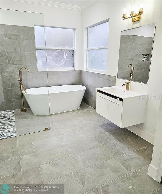 full bath with vanity, a freestanding tub, ornamental molding, a walk in shower, and tile walls