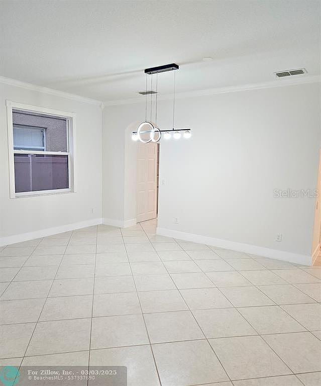 unfurnished room featuring light tile patterned floors, visible vents, baseboards, and ornamental molding