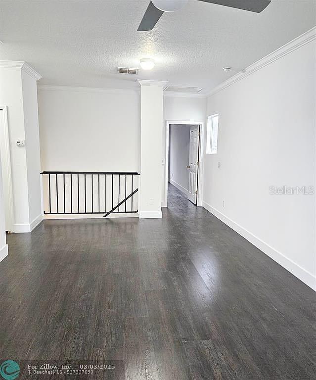 empty room with visible vents, ornamental molding, a textured ceiling, wood finished floors, and baseboards