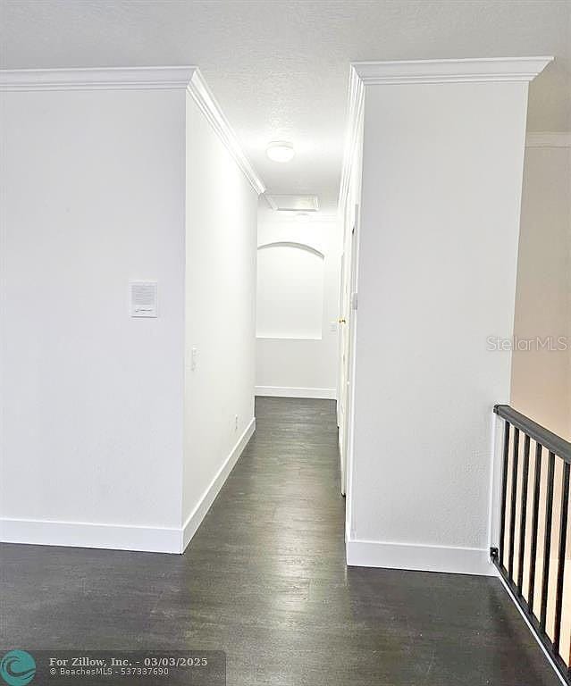 hall featuring baseboards, a textured ceiling, ornamental molding, and dark wood-style flooring