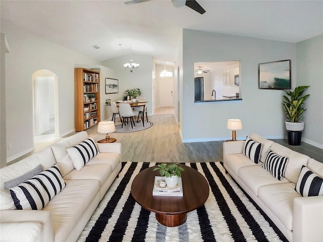 living area featuring wood finished floors, baseboards, lofted ceiling, arched walkways, and ceiling fan with notable chandelier