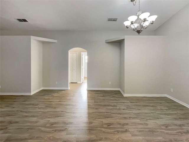 spare room with visible vents, arched walkways, baseboards, and wood finished floors