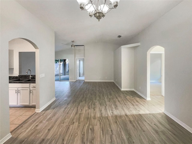 unfurnished living room with visible vents, baseboards, lofted ceiling, wood finished floors, and arched walkways