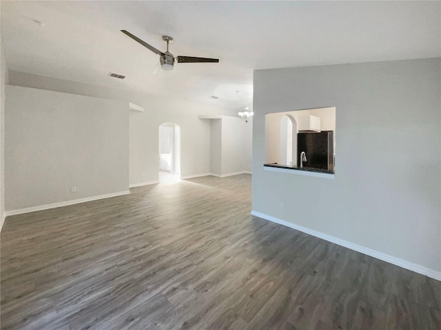 unfurnished room featuring visible vents, baseboards, dark wood finished floors, ceiling fan with notable chandelier, and arched walkways