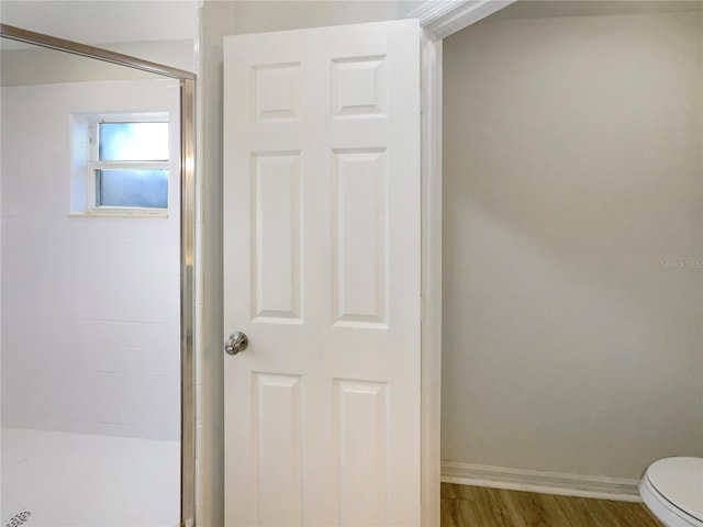 bathroom featuring a shower stall, toilet, wood finished floors, and baseboards