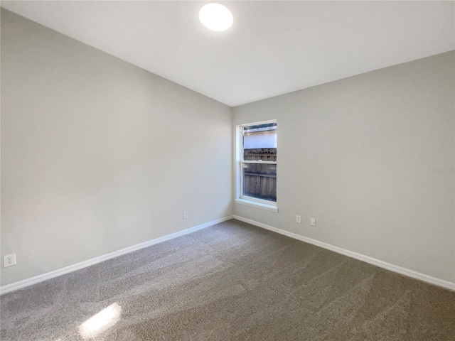 spare room featuring dark colored carpet and baseboards