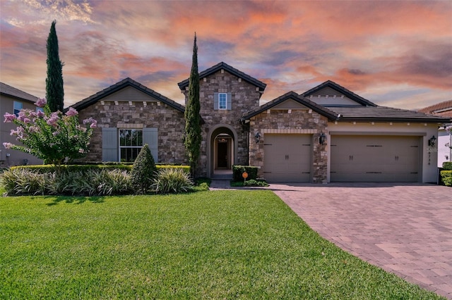 craftsman-style house with decorative driveway, stone siding, a yard, and a garage