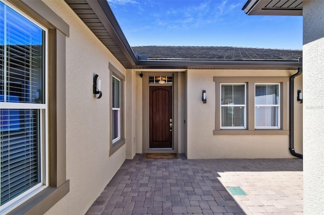 doorway to property featuring stucco siding and roof with shingles