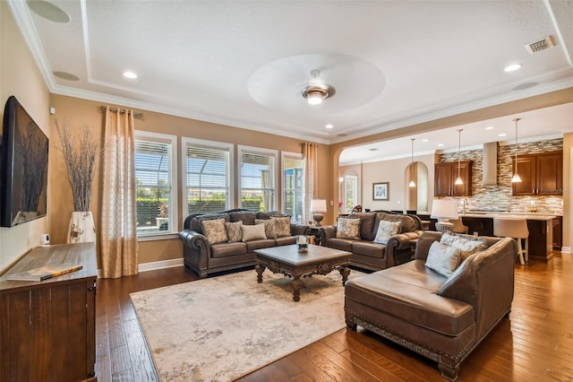 living room featuring visible vents, arched walkways, dark wood-style flooring, ceiling fan, and ornamental molding