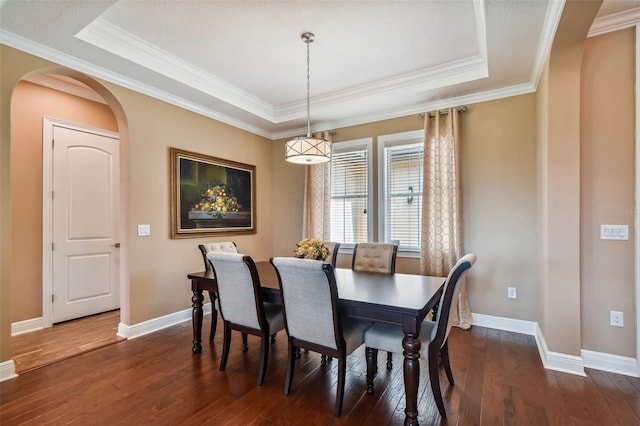 dining space with arched walkways, baseboards, dark wood-type flooring, and a tray ceiling