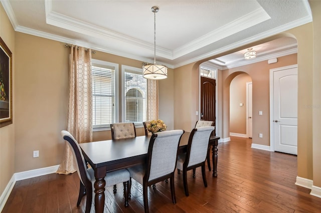 dining room with arched walkways, baseboards, a tray ceiling, and dark wood-style flooring