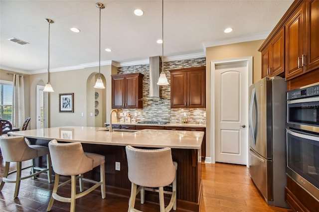 kitchen featuring visible vents, a breakfast bar, a sink, stainless steel appliances, and wall chimney range hood