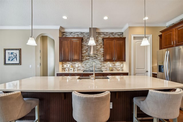 kitchen featuring a sink, backsplash, a breakfast bar area, crown molding, and wall chimney range hood