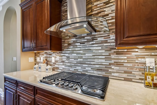 kitchen featuring light stone counters, tasteful backsplash, arched walkways, stainless steel gas stovetop, and extractor fan