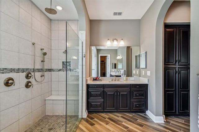 full bathroom featuring visible vents, baseboards, wood finish floors, tiled shower, and vanity