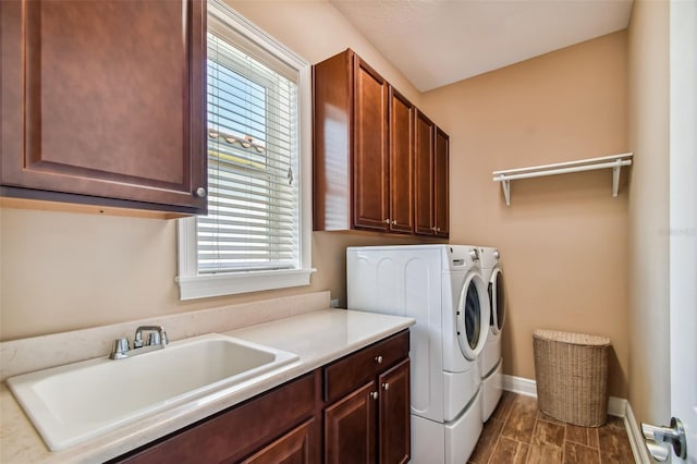 washroom with baseboards, wood tiled floor, separate washer and dryer, cabinet space, and a sink