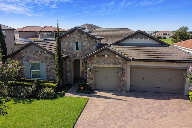 view of front of house featuring a tile roof, decorative driveway, stone siding, a front yard, and an attached garage