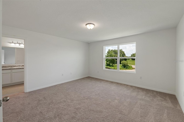 unfurnished bedroom featuring baseboards, light carpet, a textured ceiling, and ensuite bathroom