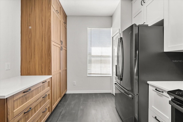 kitchen featuring baseboards, freestanding refrigerator, light countertops, black range with electric cooktop, and white cabinetry