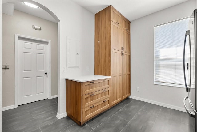 interior space featuring arched walkways, electric panel, baseboards, and dark tile patterned flooring