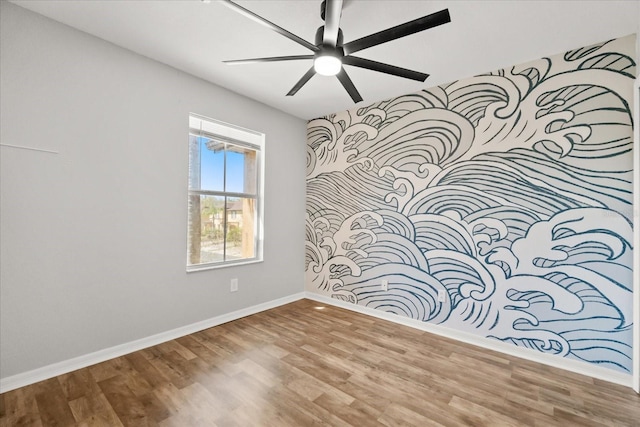 spare room with baseboards, an accent wall, a ceiling fan, and wood finished floors