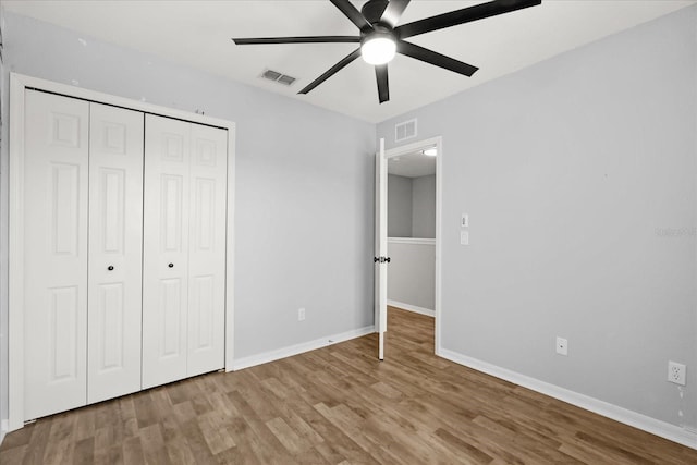 unfurnished bedroom with wood finished floors, visible vents, a closet, and baseboards