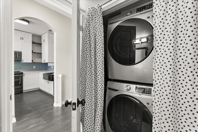 laundry room featuring arched walkways, laundry area, and stacked washing maching and dryer