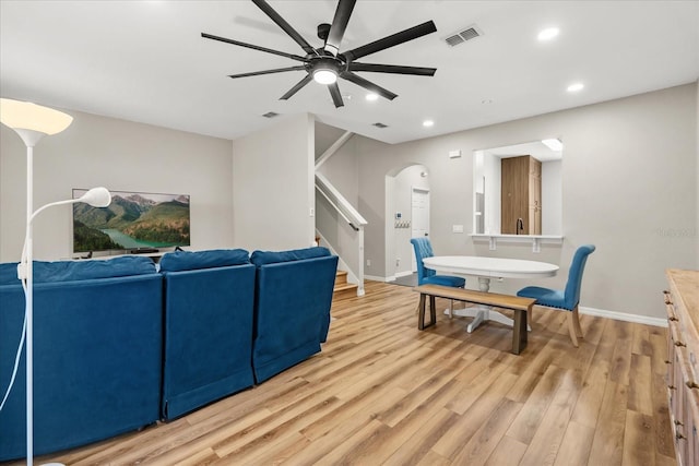 living area featuring stairway, a ceiling fan, arched walkways, light wood-style flooring, and visible vents