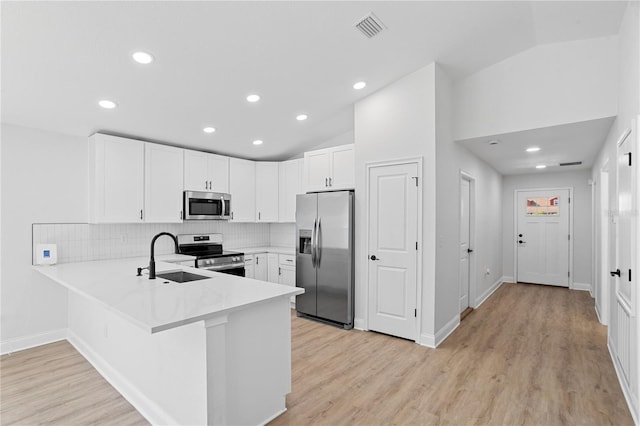 kitchen featuring light countertops, lofted ceiling, appliances with stainless steel finishes, a peninsula, and a sink