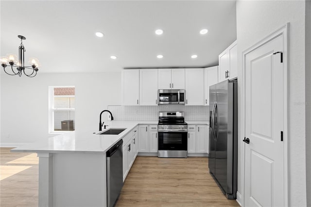kitchen with a peninsula, a sink, stainless steel appliances, light wood-style floors, and a notable chandelier
